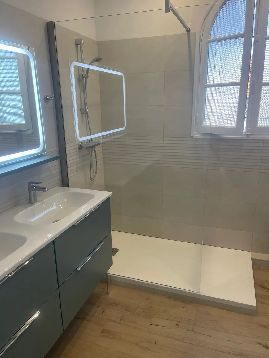 Après travaux — Grès cérame grand format et douche à l'italienne sous la fenêtre cintrée d'origine, sol effet bois et double vasque.