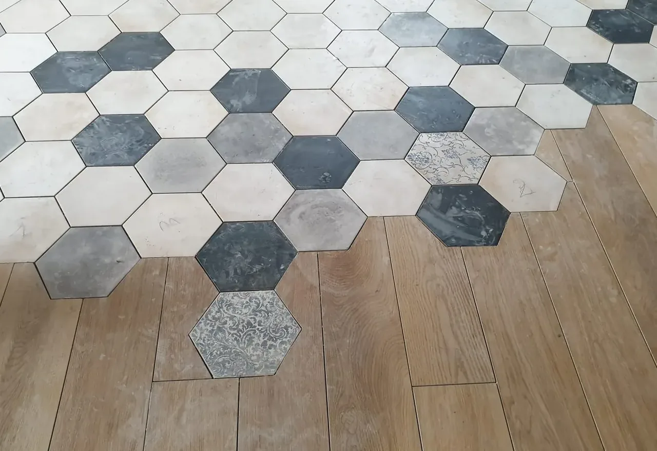 Calepinage en transition : tomettes hexagonales fondues dans un parquet céramique, pose Atout Carrelage